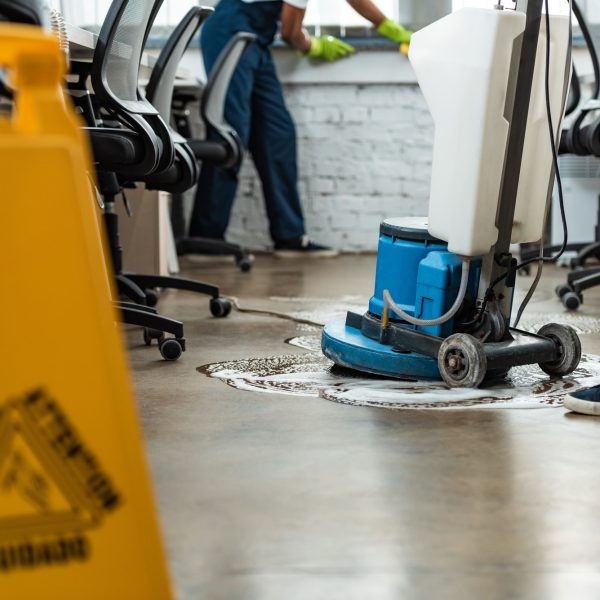 cropped view of cleaner washing floor with cleaning machine near colleague